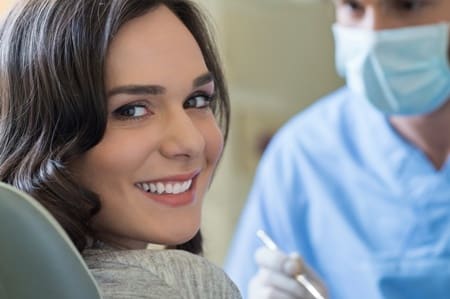 Woman in detail operating chair looking back smiling as dentist prepares to do dental work